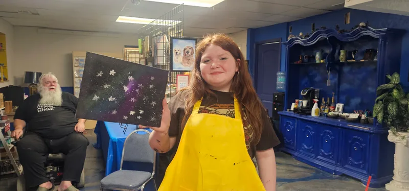 A young painter holding up the canvas she finished